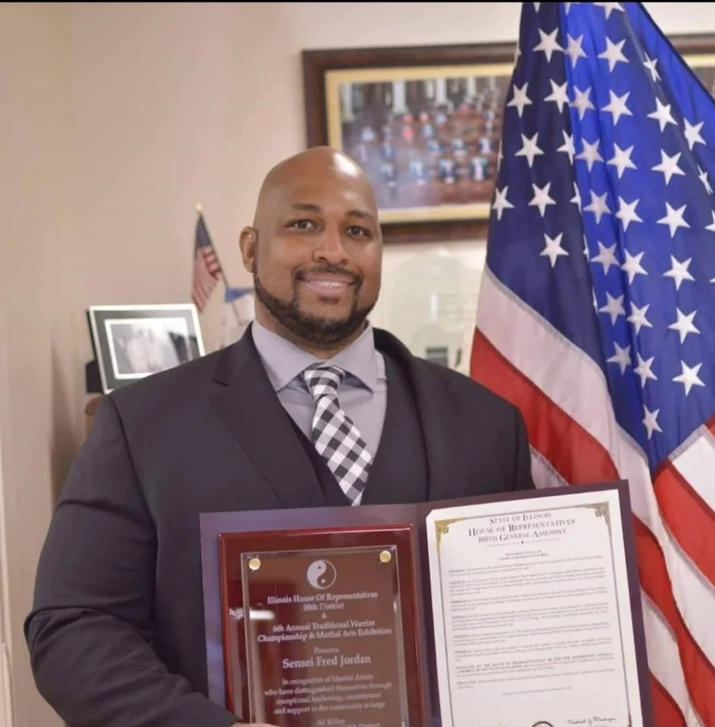 Formal photograph of Fred Jordan displaying plaques and a certificate of recognition